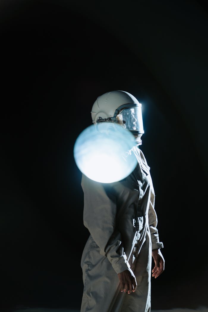 Astronaut standing in space suit with dramatic light reflection against dark background.